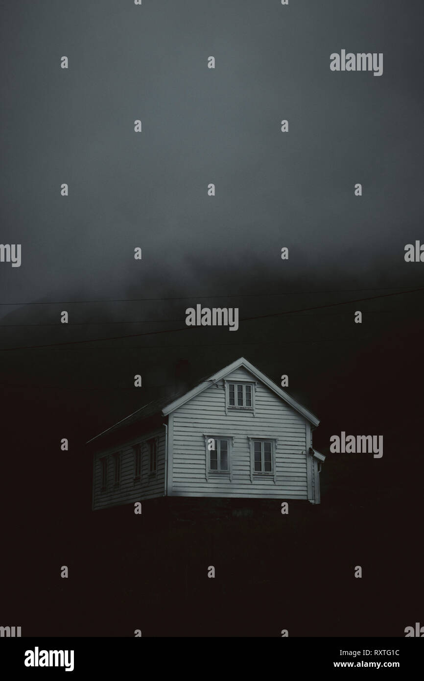 Un solitario fantasmal casa blanca en un oscuro paisaje de nubes bajas. Foto de stock