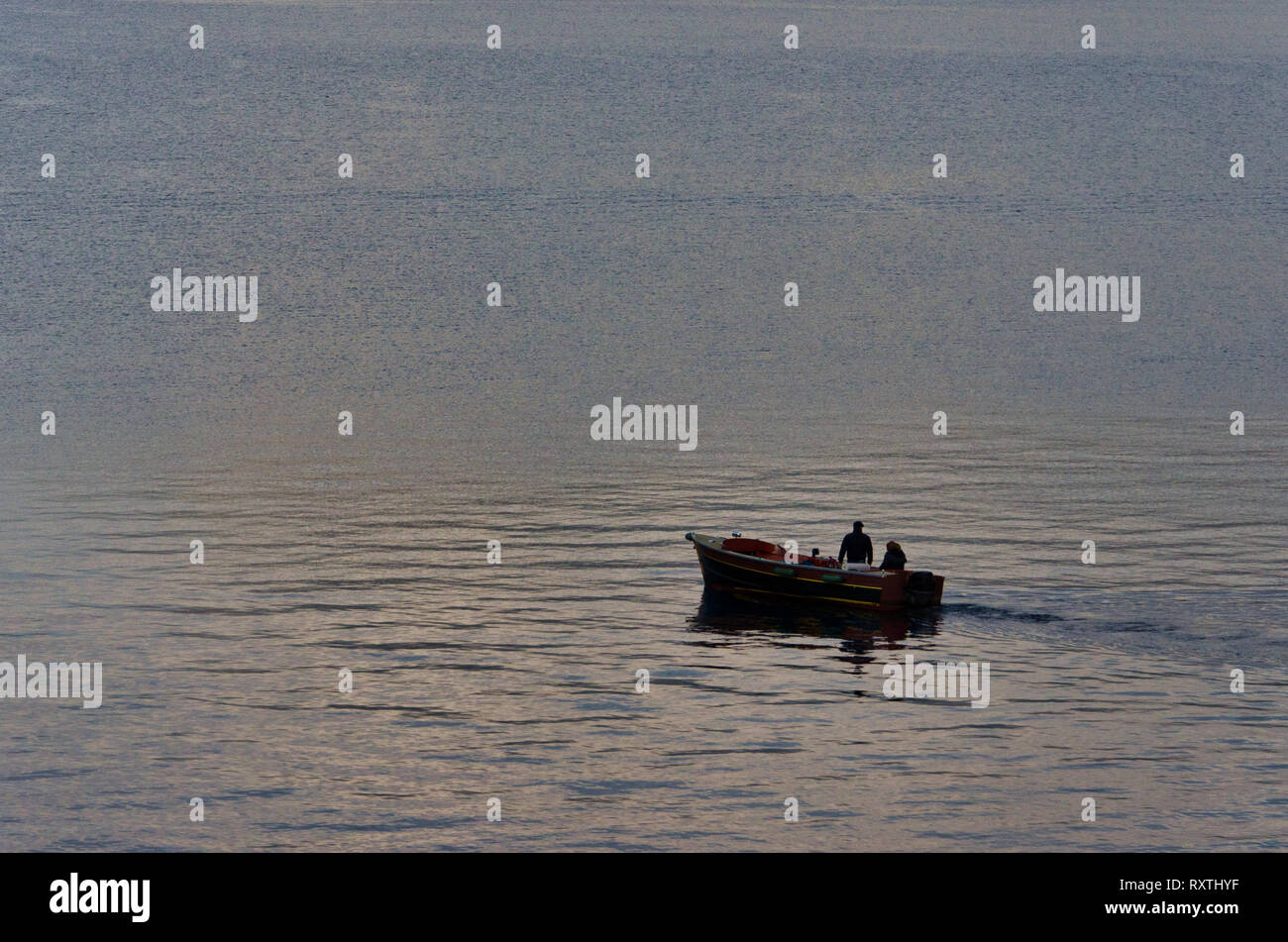 Pequeño barco con dos pescadores en el lago, la reflexión de la luz sobre el agua, el agua de superficie rugosa, tranquilo escenario del lago de Iseo en Italia Foto de stock