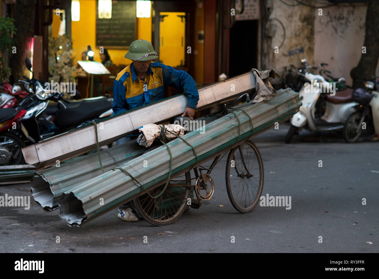 Hombre con barras de metal de hoja para su entrega en una bicicleta en una  calle de Hanoi. La gente vietnamita se utilizan para cargar y transportar  un montón de cosas en