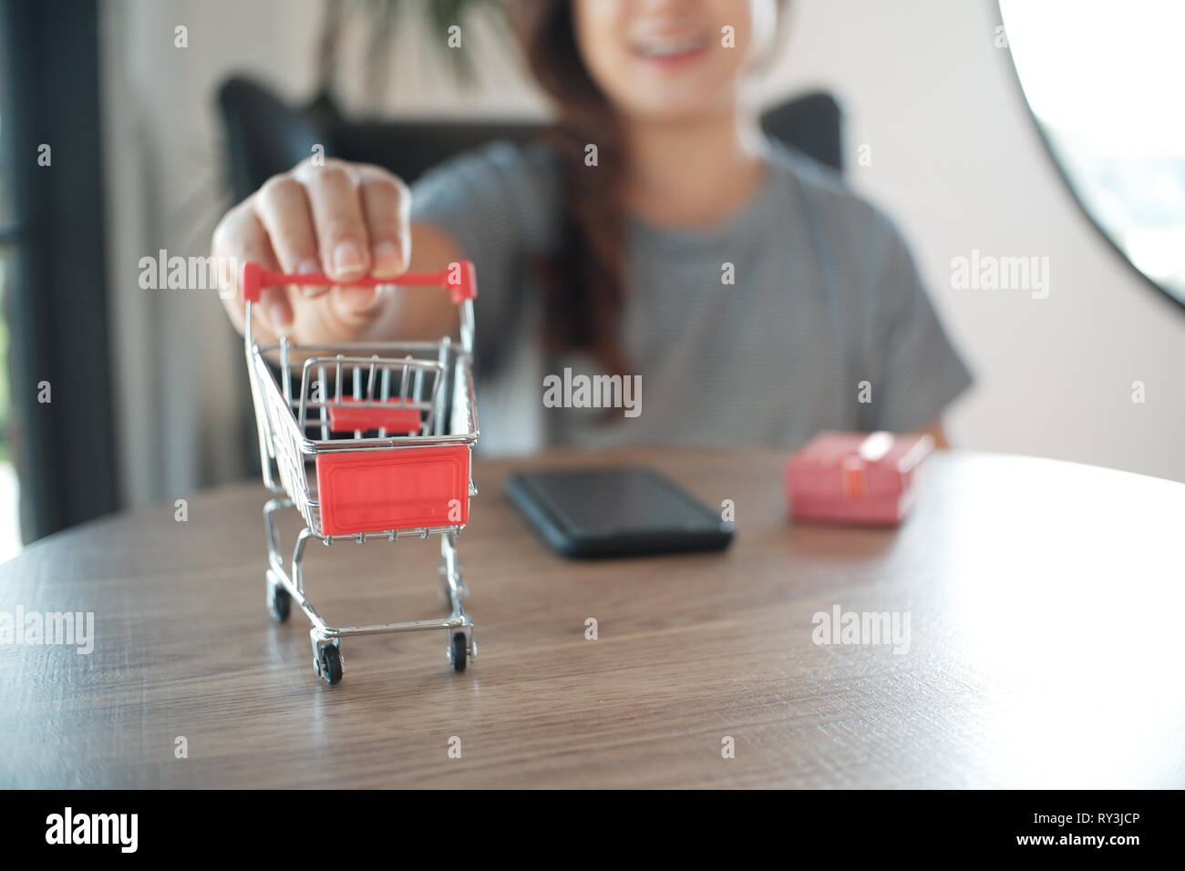 Cerca de miniatura compras /trolley toy figura. smart phone y caja de regalo roja sobre la mesa para ir de compras y el concepto de e-commerce Foto de stock