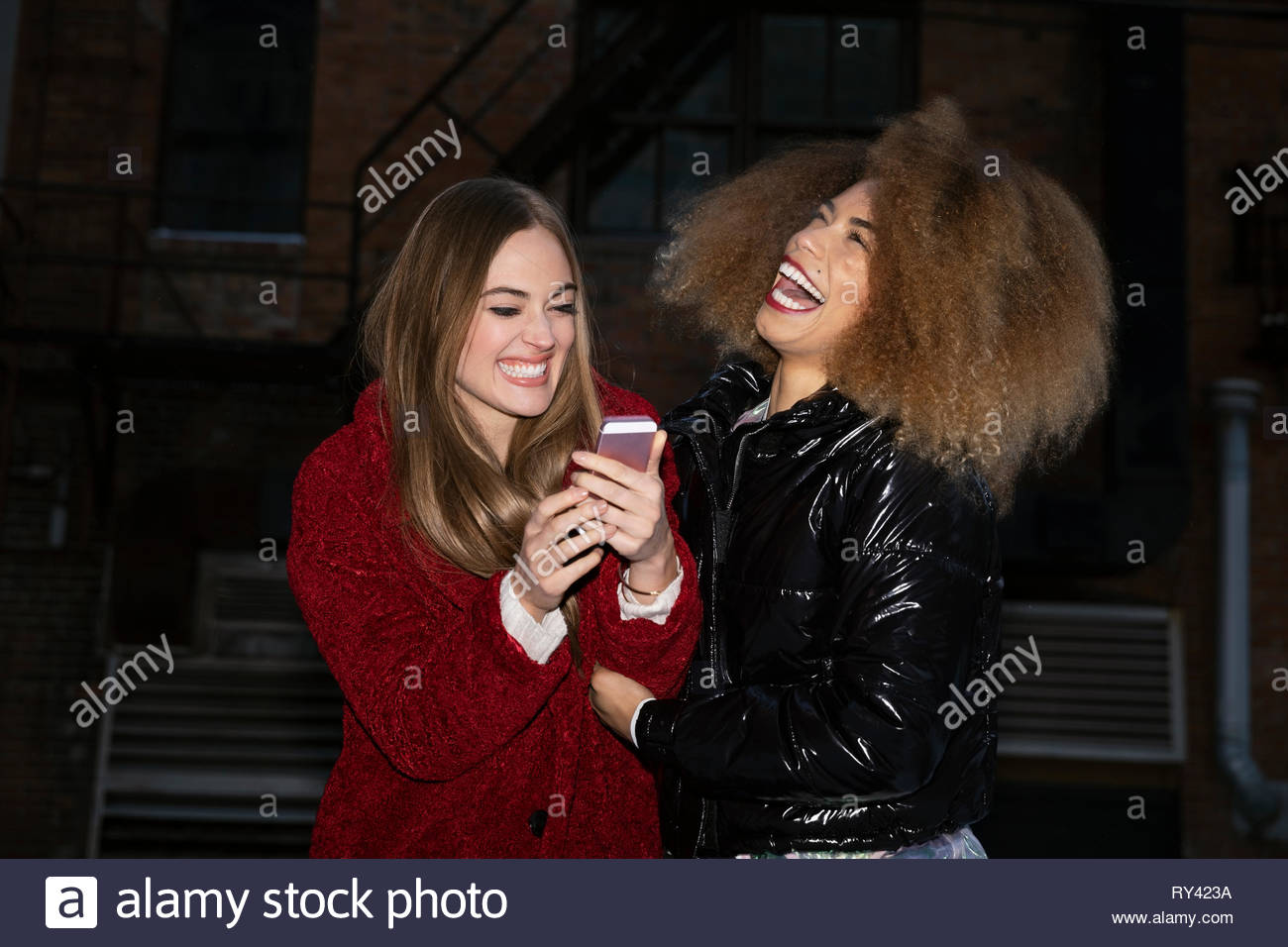 Laughing mujeres jóvenes amigos con smart phone en calle urbana Foto de stock
