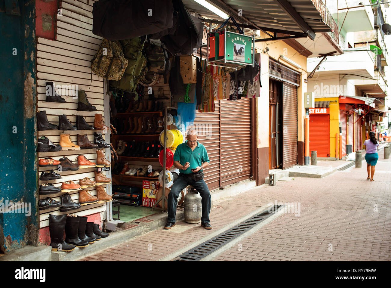 Tendero local comprobando su móvil fuera de su tienda de ropa exterior. La  Avenida Central, centro de la Ciudad de Panamá, Panamá, América Central.  Oct 2018 Fotografía de stock - Alamy