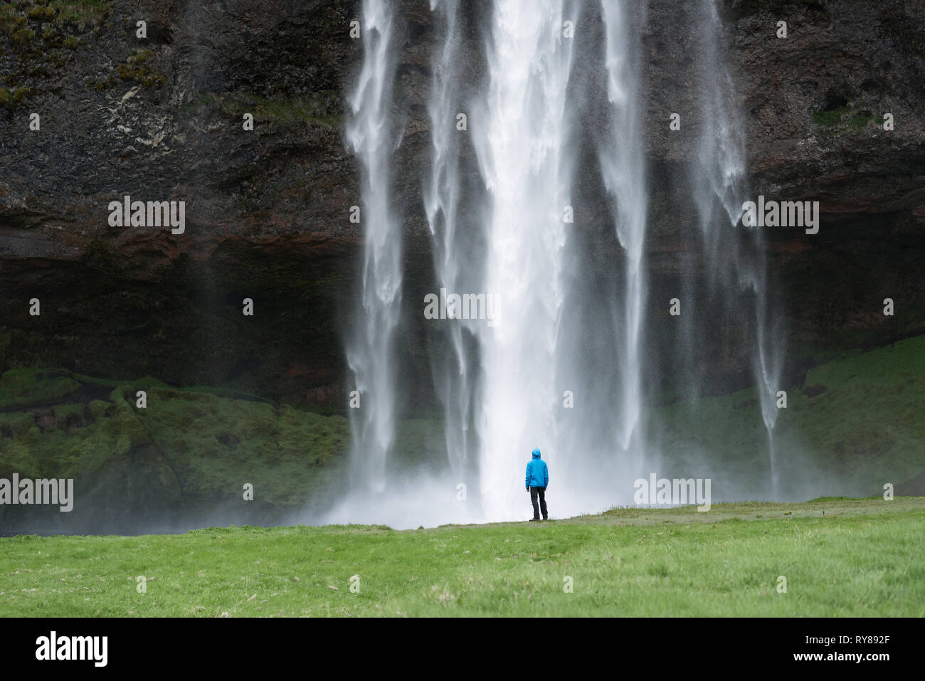 Selyalandfoss cascada en Islandia. Turista en chaqueta azul mira el enorme flujo de agua. Hermoso monumento natural Foto de stock