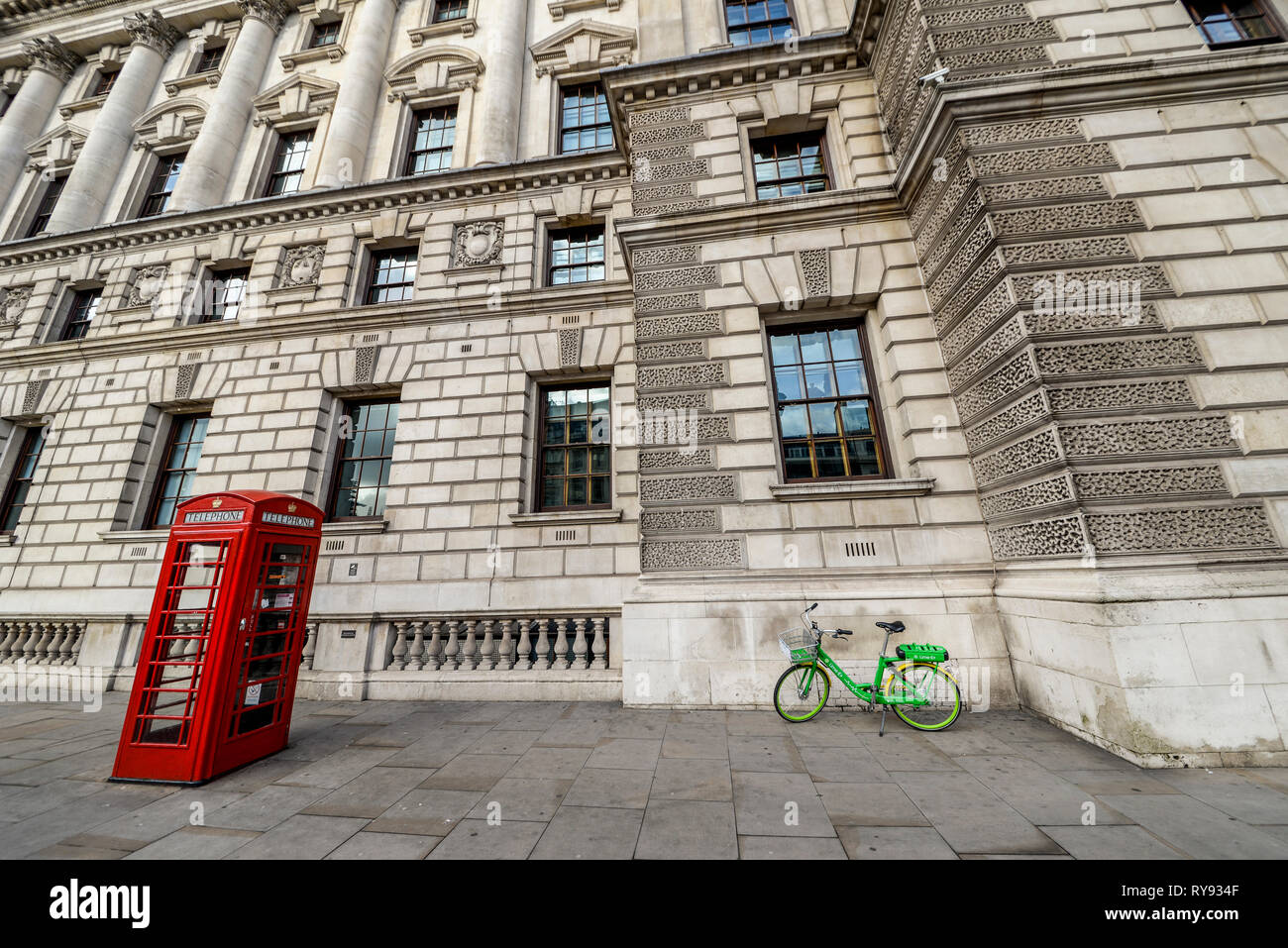 Escena londinense, caja del teléfono rojo y verde lima e alquiler eléctrico esquema bicicleta bicicleta dejó fuera del edificio de gobierno en Whitehall, Londres, Reino Unido. Foto de stock