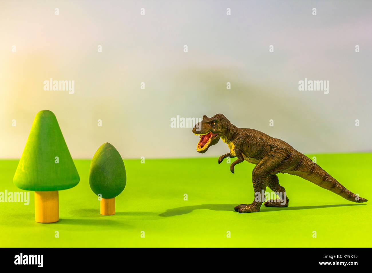 Dinosaurio de juguete en un juguete bosque. Como un verdadero dino en un bright studio fondo con árboles de madera.Eco juguetes. Foto de stock