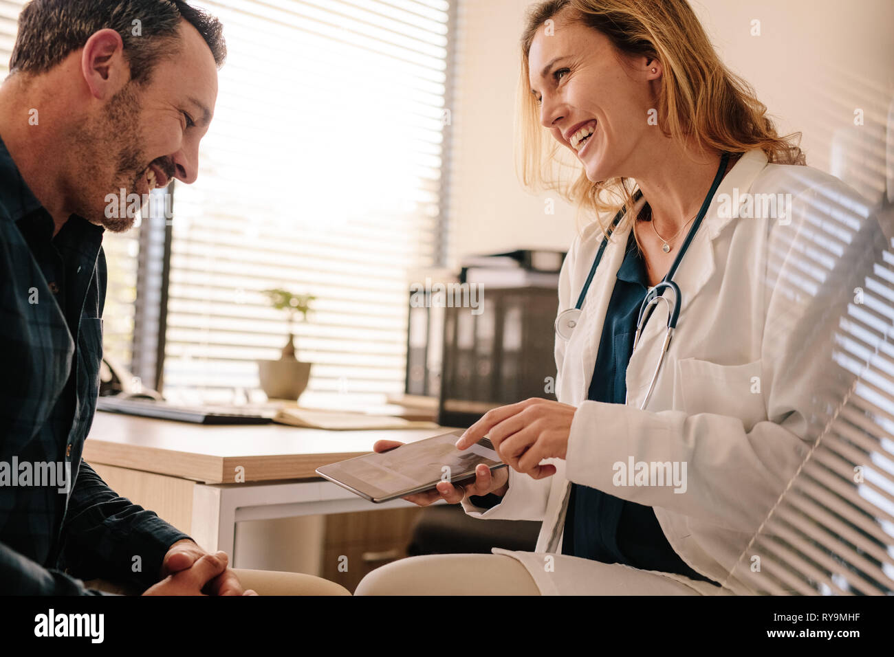 Doctora mostrando buenos resultados de prueba a un paciente masculino. Profesionales médicos sonrientes compartir buenos resultados con su paciente. Foto de stock