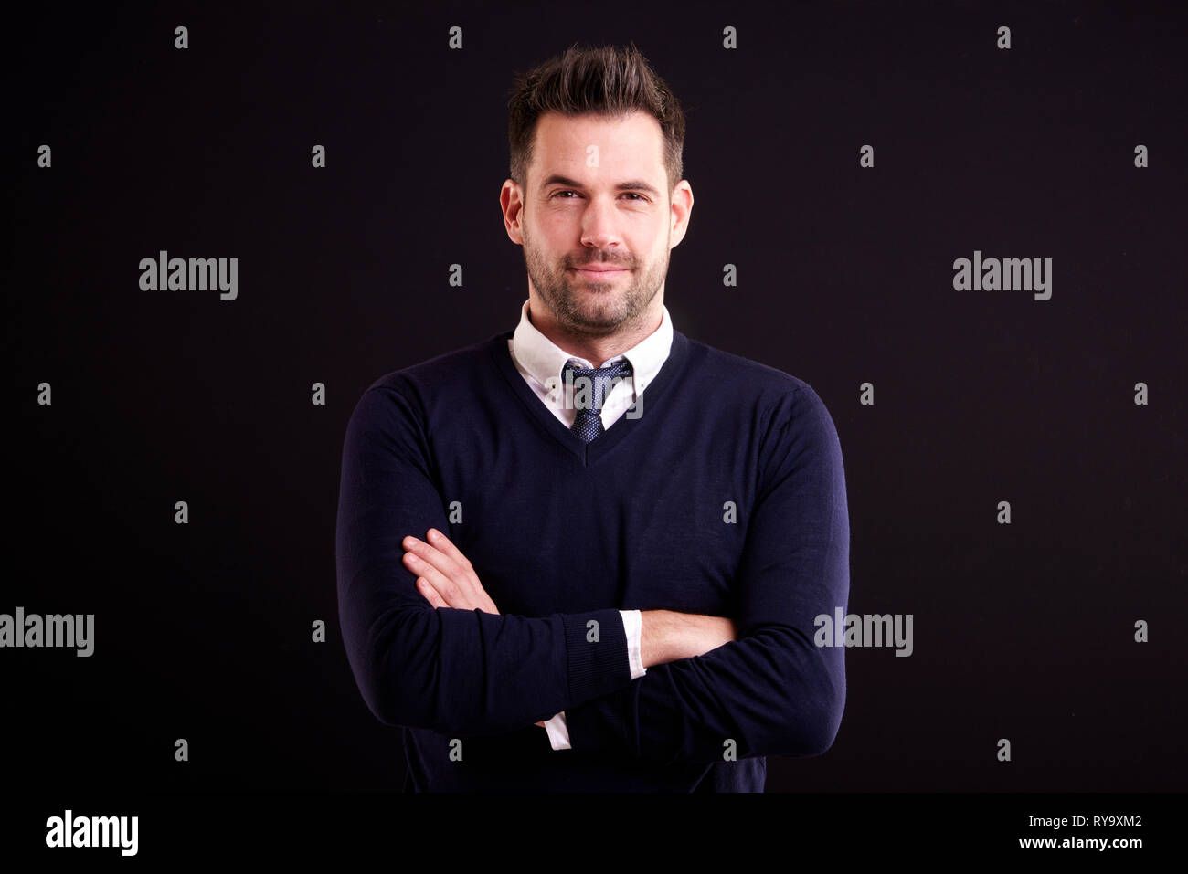 Retrato de estudio de seguros empresario vistiendo camisa y corbata con  suéter mientras está de pie con los brazos cruzados en fondo negro aislado  Fotografía de stock - Alamy