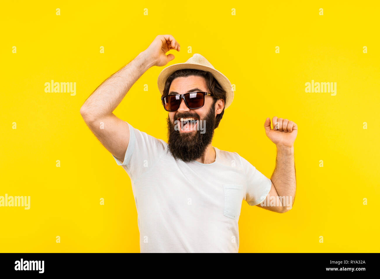 Retrato de estudio de un hombre barbado con un estado de ánimo positivo, un  chico de gafas de sol es el baile arco iris sobre un fondo amarillo, el  concepto de una