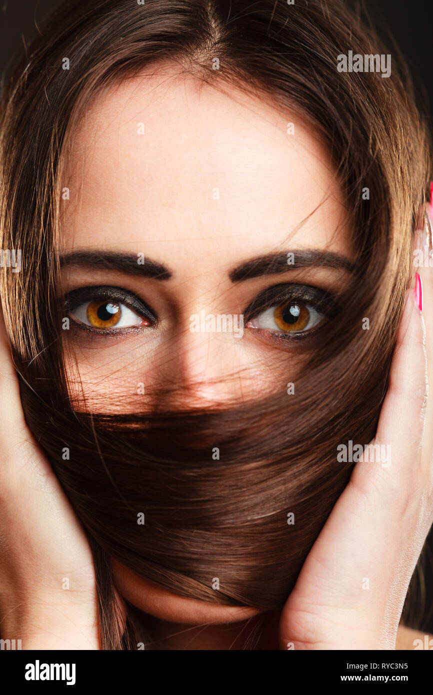 Cerrar mujer cubre el rostro por largos pelos marrones ojos marrones con maquillaje oscuro Foto de stock
