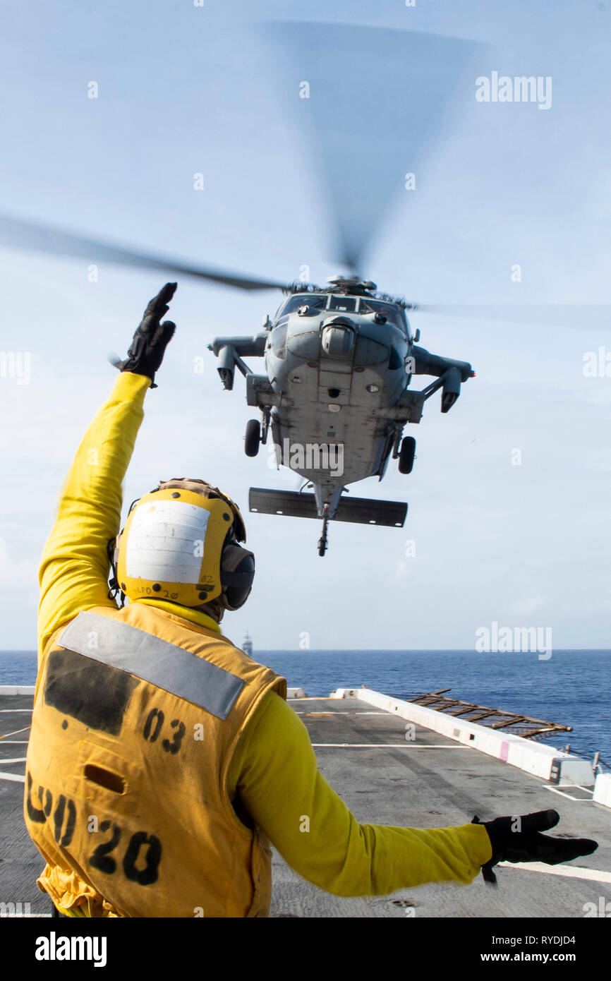 190311-N-DX072-1137 OCÉANO PACÍFICO (11 de marzo, 2019) - Aviacion Boatswain's Mate (manejo) Aviador Caleb Brawner, de Wichita, Kansas, señales a un SH-60 Sea Hawk helicóptero asignado a la Isla de los Caballeros de mar escuadrón de helicópteros de combate (HSC) 25 como se despega de la cubierta de vuelo del buque anfibio de transporte dock USS Green Bay (LPD 20) durante un ejercicio de entrenamiento con otros buques de guerra de la Marina de los EE.UU. Los buques de guerra de la Marina de EE.UU. entrenan juntos para aumentar la habilidad táctica, la letalidad y la interoperabilidad de las unidades participantes en una época de gran potencia para la competencia. (Ee.Uu. Navy photo by Mass comuni Foto de stock