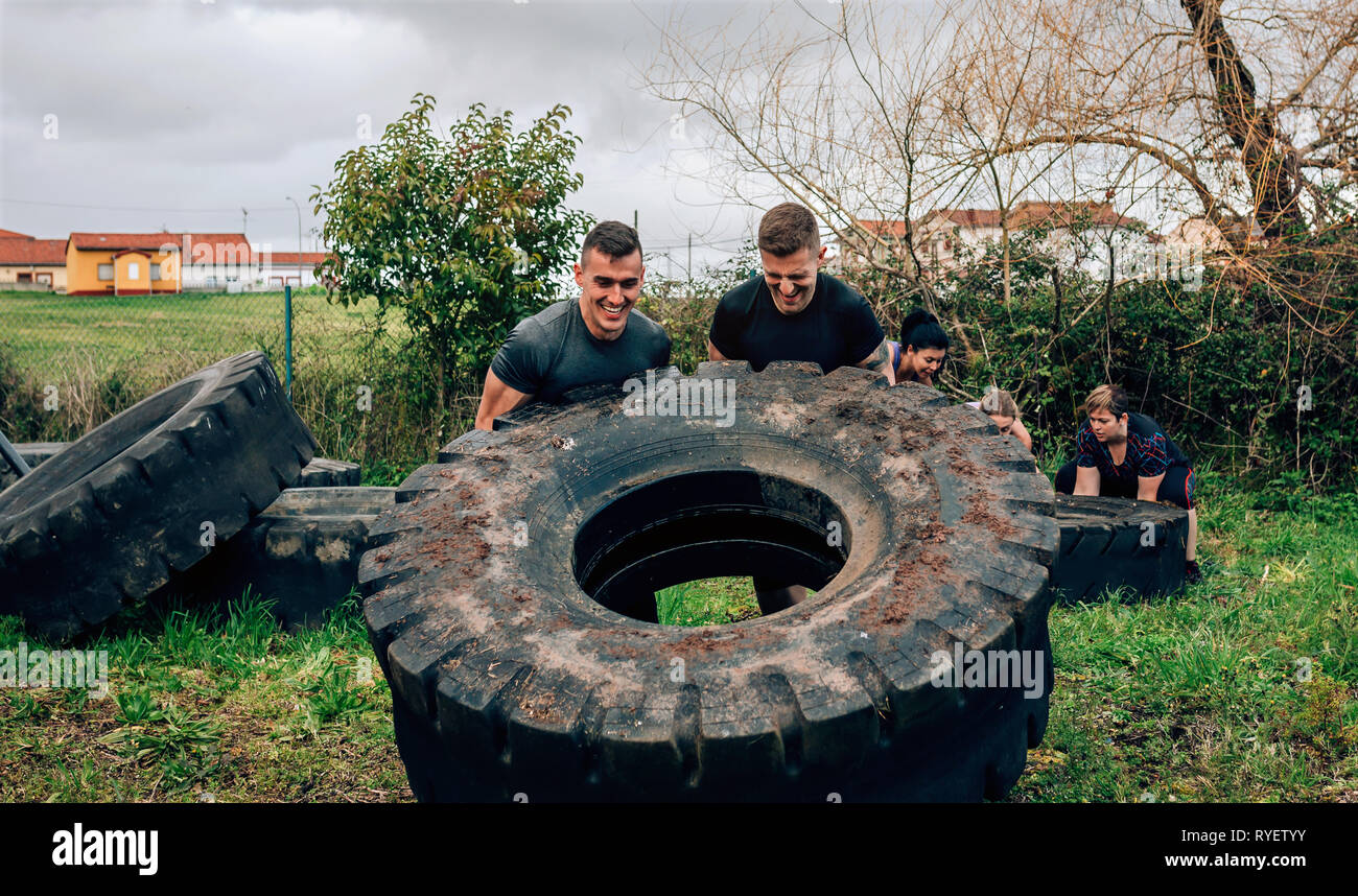 Los participantes en una carrera de obstáculos girando una rueda Foto de stock