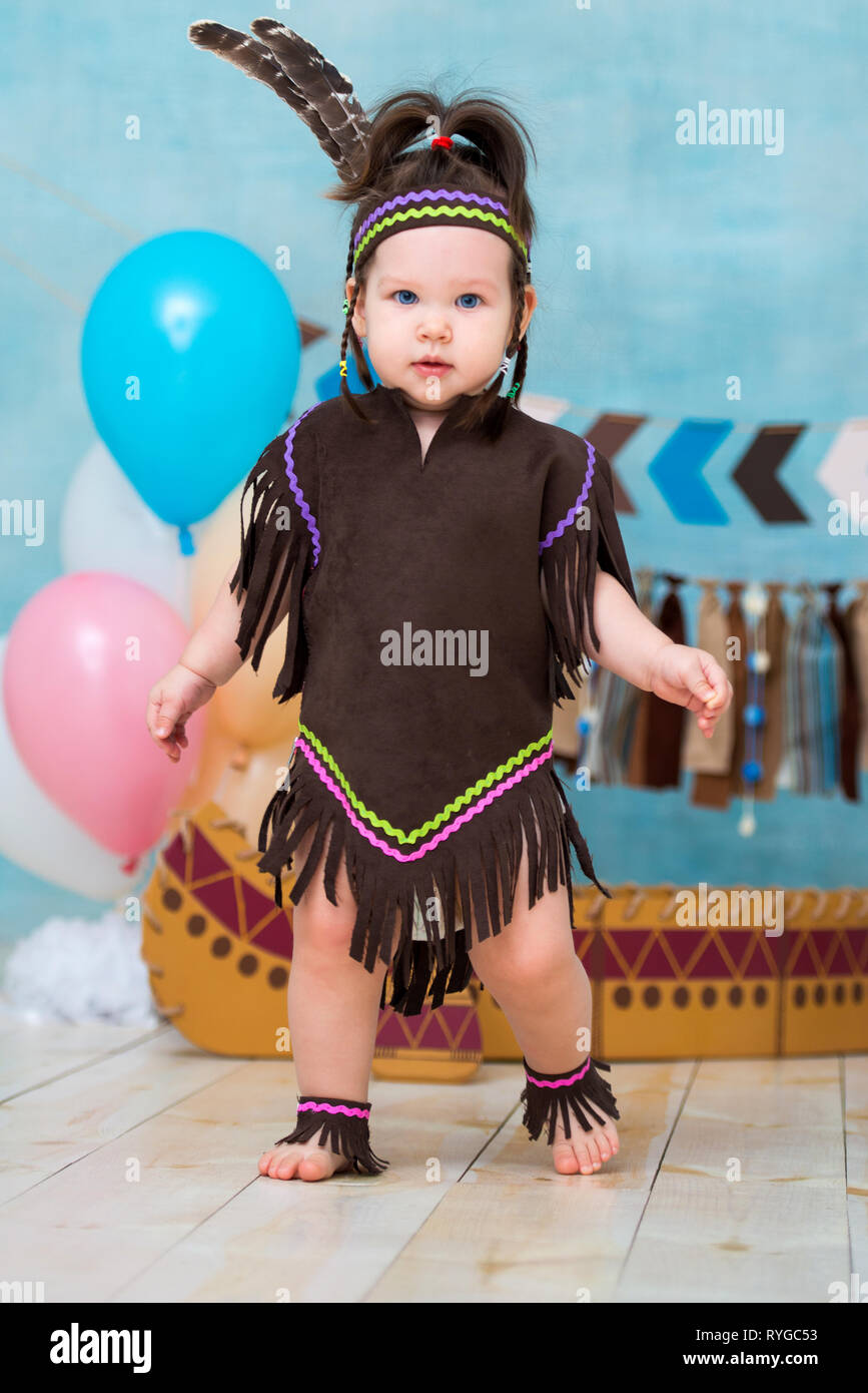 Cute Little Girl en traje de Apache jefe indio y un tocado de plumas se  asienta en canoa. Primer cumpleaños de vacaciones para niños y Smash torta  1 año Fotografía de stock -