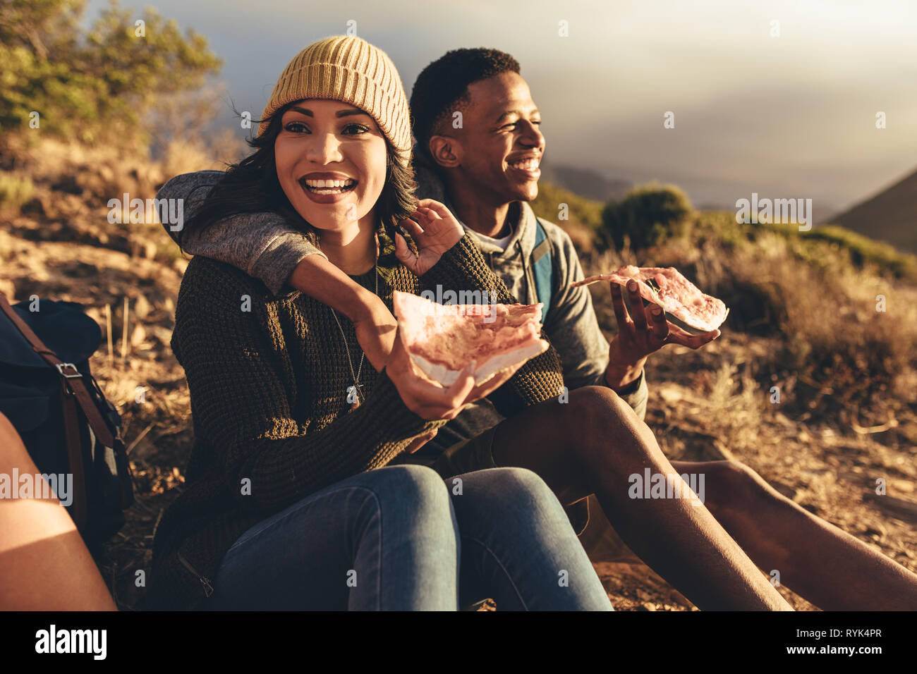 Dos amigos que pizza sentados en camino de montaña. El hombre y la