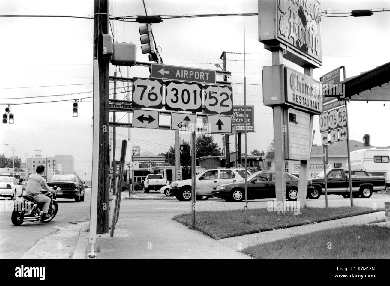 Jacksonville, Carolina del Norte, EE.UU. 90. Down Town iIntersection ocupado con moto rider, girando a la derecha y no llevar un casco de seguridad. Numerosas coches y los carteles de la calle.1999 90s USA HOMER SYKES. Foto de stock