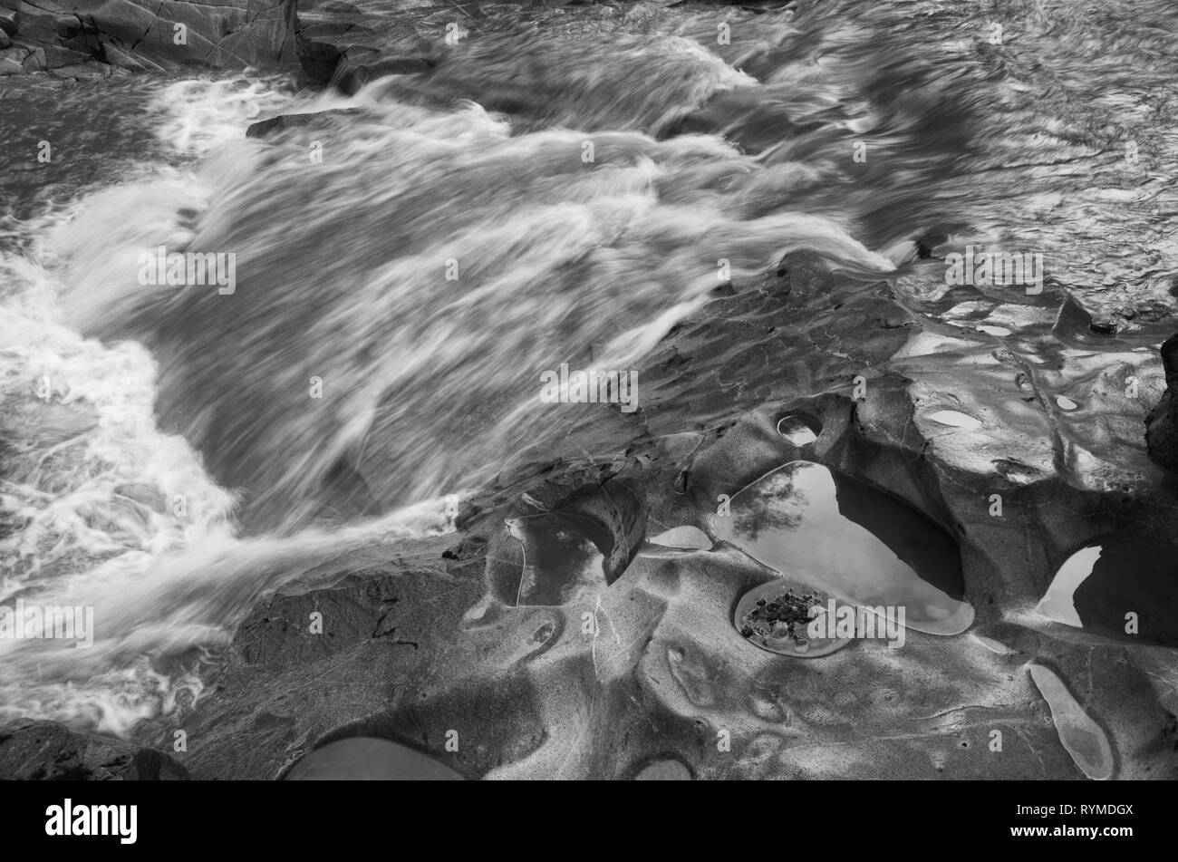 La larga exposición en negro en blanco muestra el movimiento rápido del agua y el detalle de la cama de roca. Foto de stock