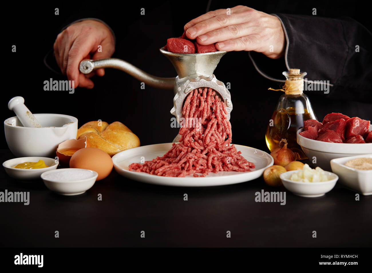 https://c8.alamy.com/compes/rymhch/hombre-picar-la-carne-con-la-amoladora-manual-en-black-mesa-de-la-cocina-visto-de-cerca-entre-platos-con-ingredientes-de-cocina-rymhch.jpg