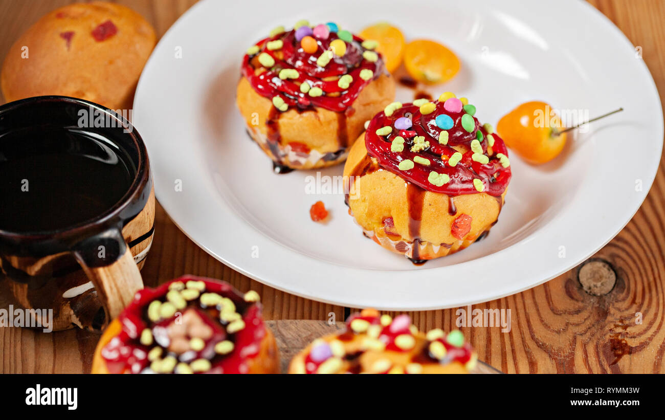 Aderezado muffins con los ingredientes de un caramelo, jalea y jarabe de chocolate oscuro con café en la placa colocada sobre la mesa de madera. Foto de stock