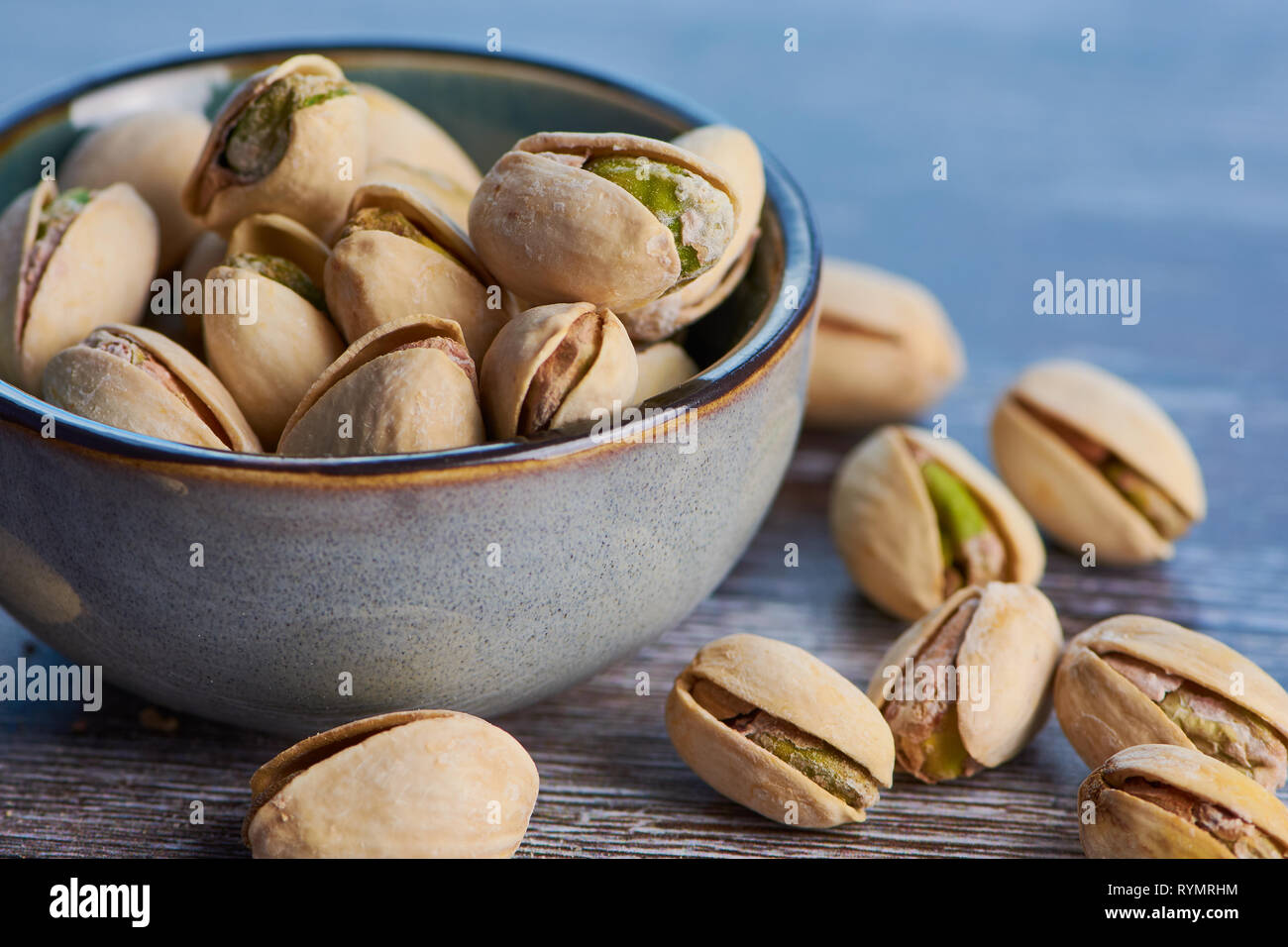 Cerca de pistachos imágenes en color tostado y salado en un cuenco de cerámica sobre una superficie de madera Foto de stock
