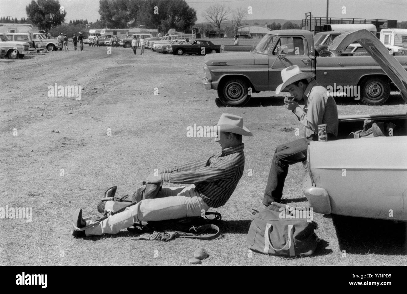 Evanston Wyoming USA 1970. Dos jóvenes vaqueros, preparándose para un rodeo  en el aparcamiento. Un vaquero se sienta en una silla de caballo que está  en el suelo y finge que está