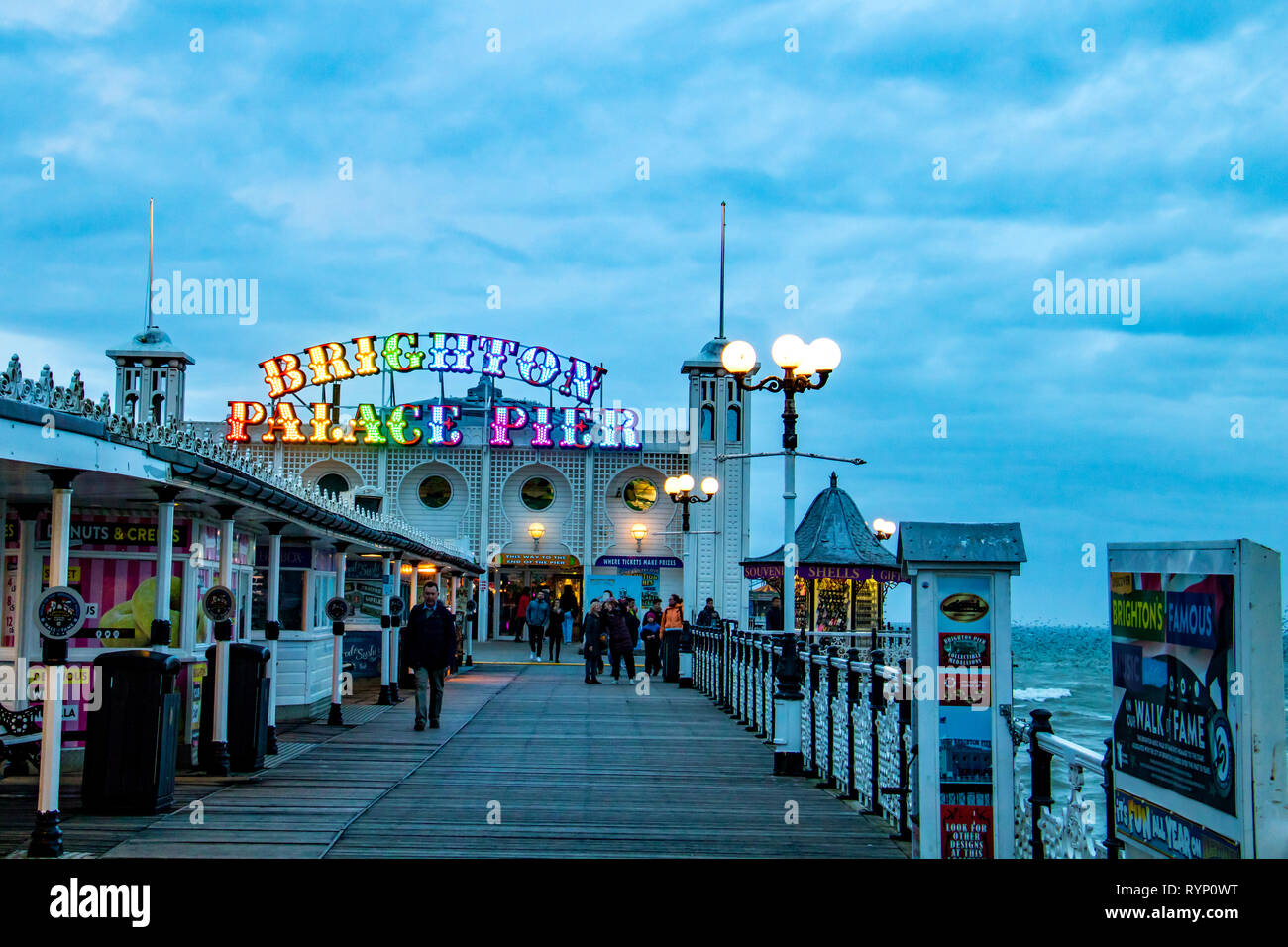 La gente pasea en Brighton Palace Pier en la noche con su colorido cartel brillando en la intensidad de la luz Foto de stock