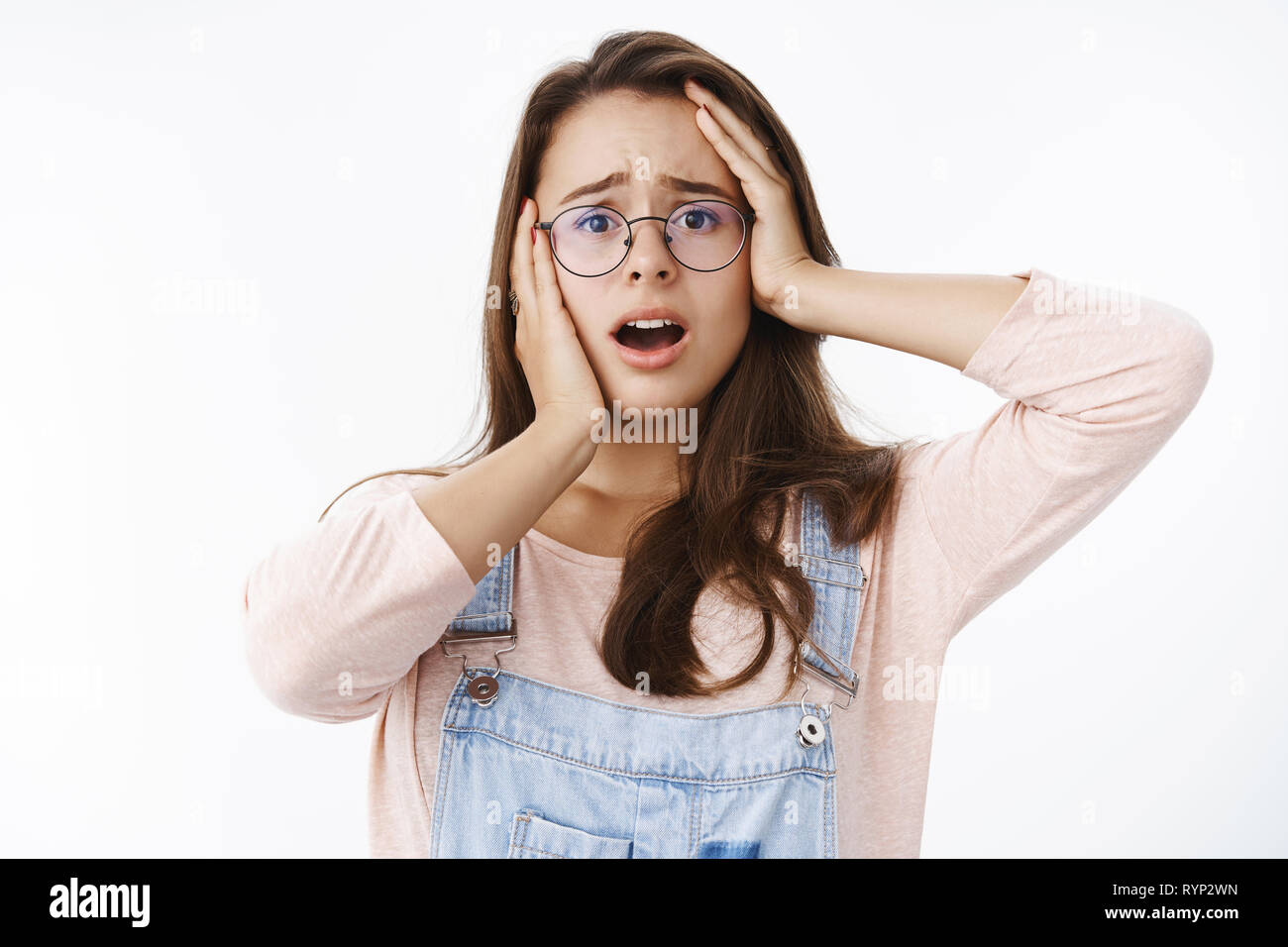 Cintura-up shot preocupada cute brunette femenino sentir empatía y shock abierta la boca y fruncir el ceño en la desesperación, tomados de las manos en la cabeza presenciando terribles Foto de stock