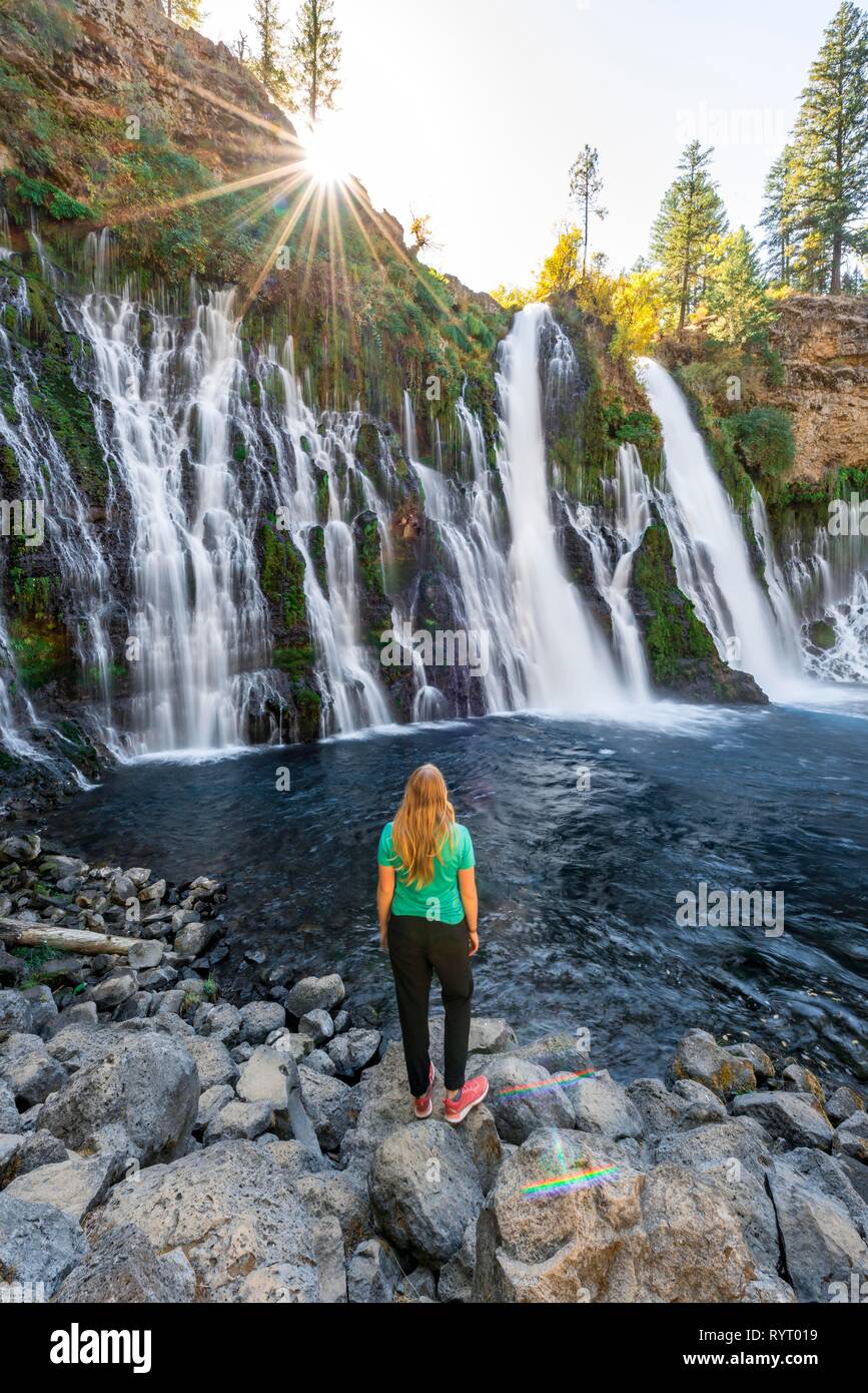 Mujer joven de pie al lado de una cascada, McArthur-Burney cae Memorial State Park, California, EE.UU. Foto de stock