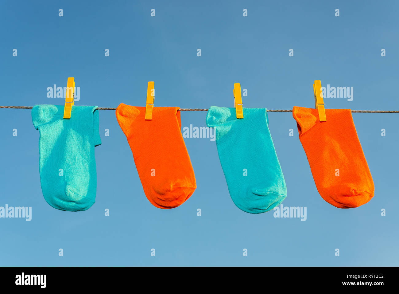 Cuatro nuevos, limpios, lavados Calcetines azul y naranja colgando en una cuerda con clothespins amarillo azul cielo. Foto de stock