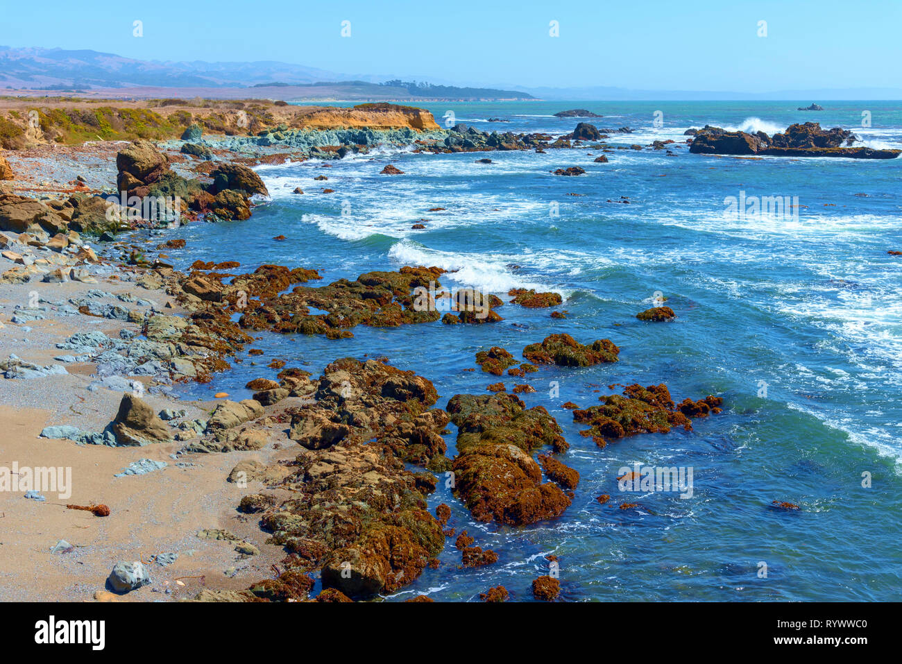 Litoral rocoso con las olas rompiendo contra las rocas bajo un cielo azul. Foto de stock