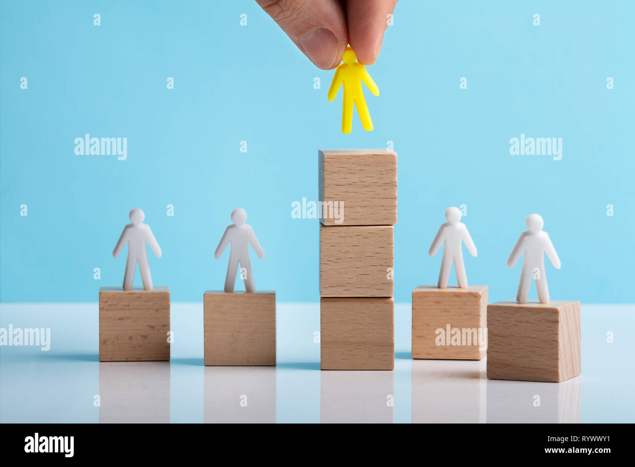 Mano colocando figura humana sobre el bloque de madera apilados en el escritorio blanco Foto de stock