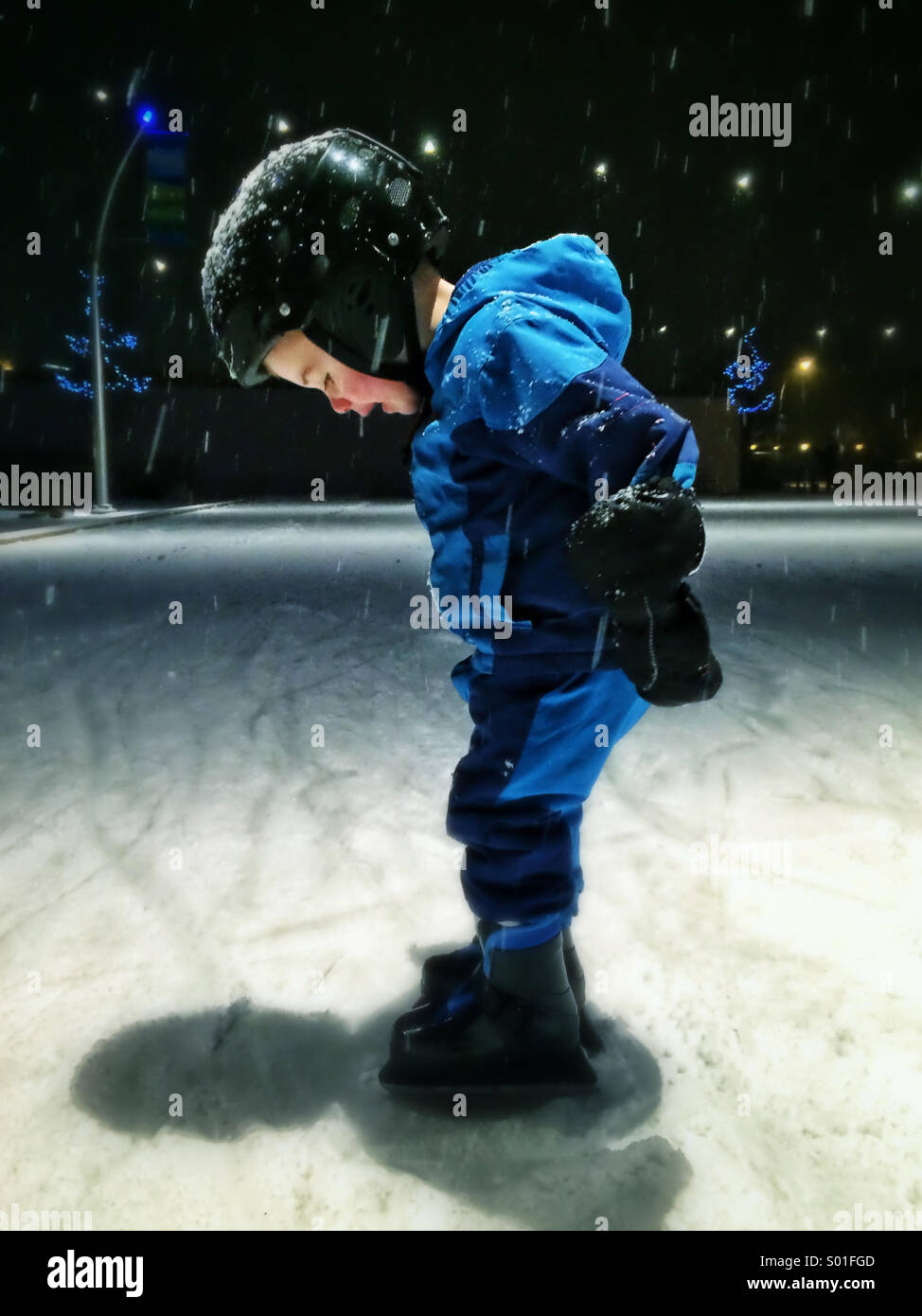 Niño aprender a patinar en la pista de patinaje al aire libre con casco Foto de stock