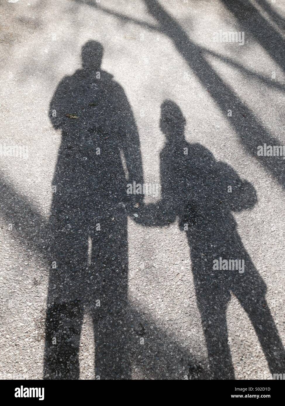 Sombra del niño y de los padres, los géneros no están claros podría ser padre, madre, hijo o hija. El niño está sosteniendo un balón bajo el brazo. La superficie es de asfalto. A comienzos de la primavera (marzo), Londres, Reino Unido. Foto de stock
