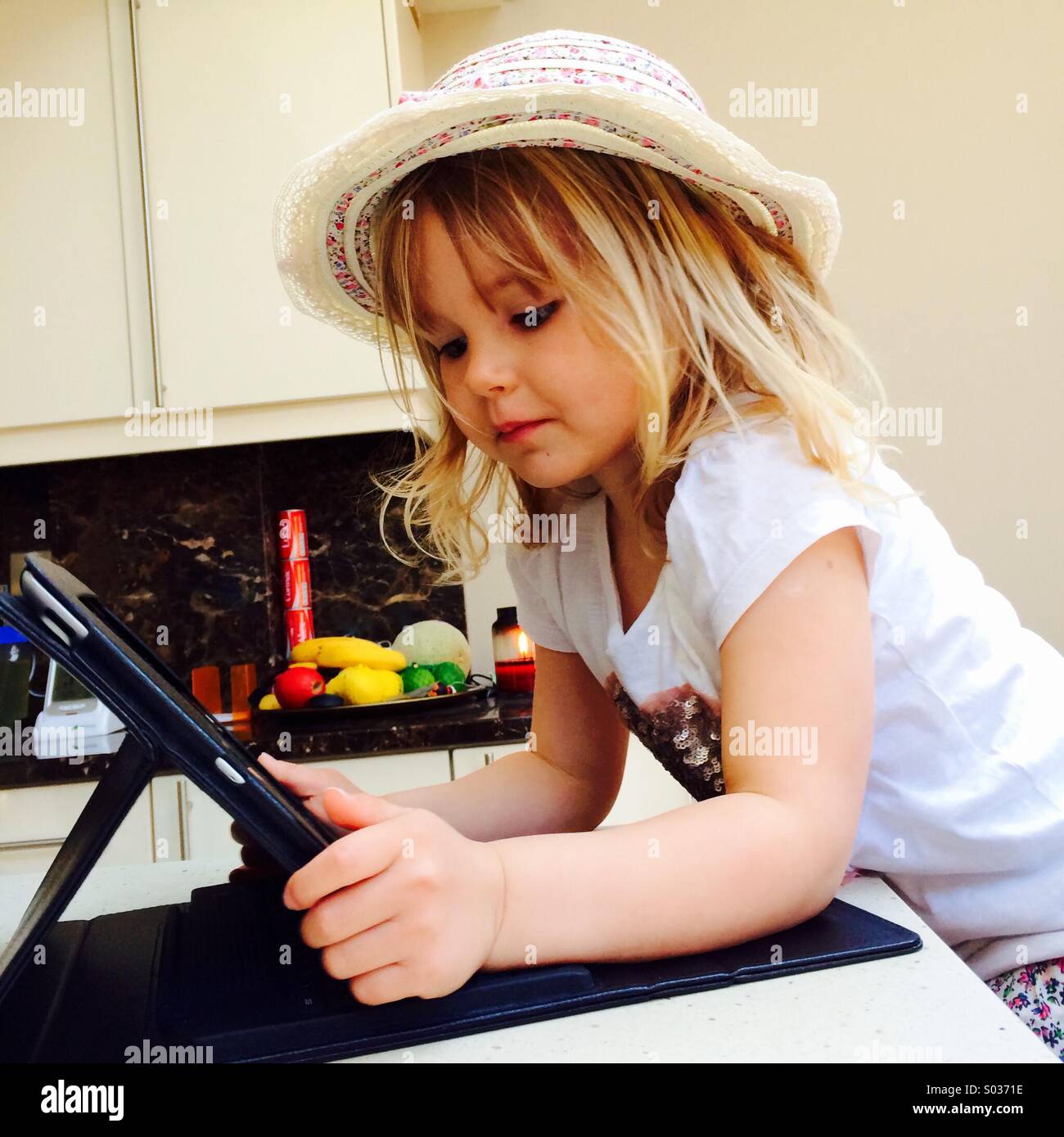 La pequeña niña con sombrero mirando a un iPad Foto de stock
