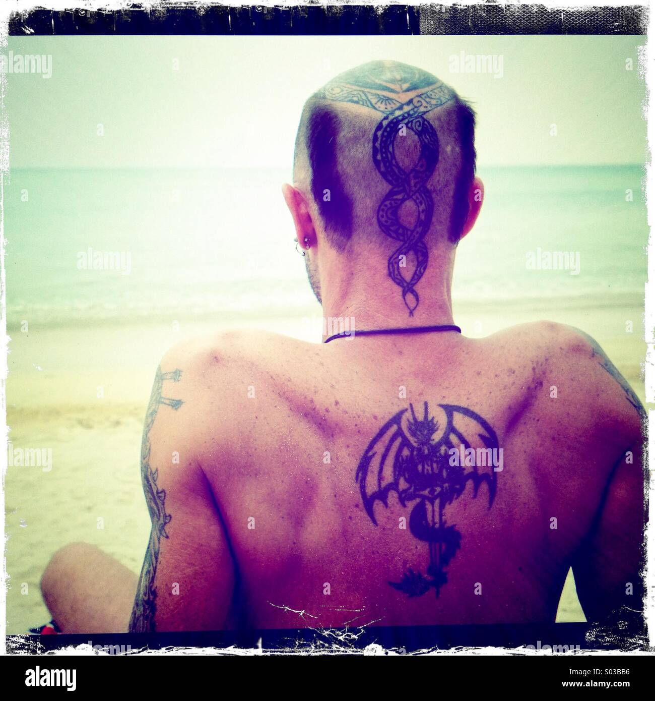 Vista posterior del hombre con tatuajes en la playa Foto de stock