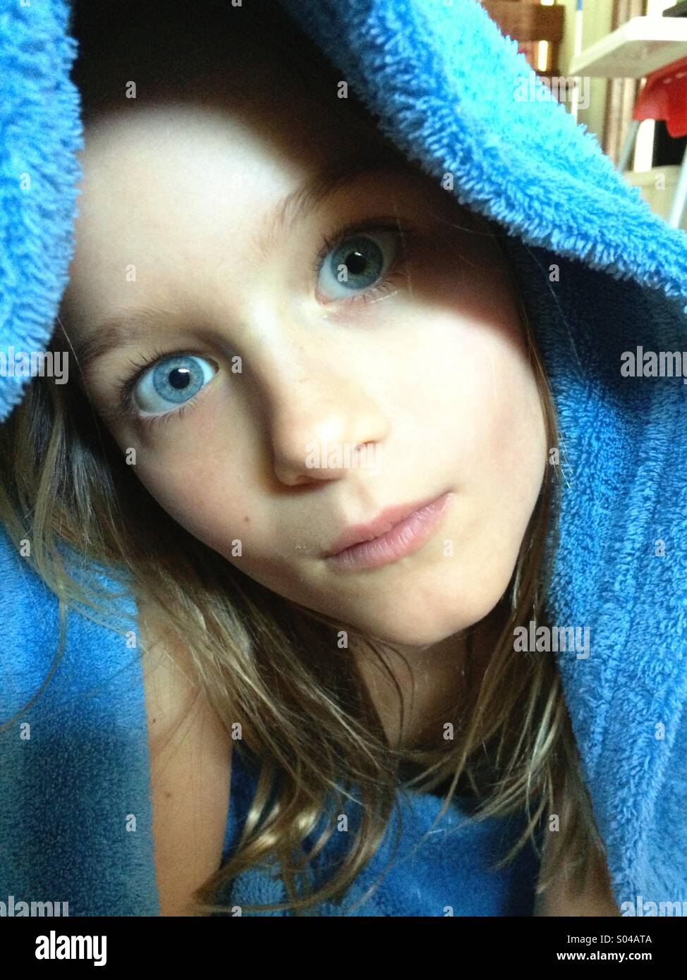 Chica joven con ojos azules cubiertos con la manta azul mirando la cámara Foto de stock