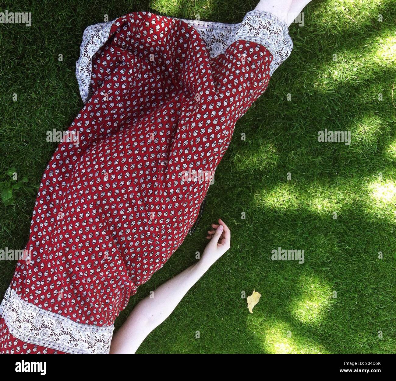 Una joven en un vestido rojo estampado radica soñar bajo las sombras de los  árboles, al lado de una sola hoja, caído sobre un manto verde de césped en  un hermoso día