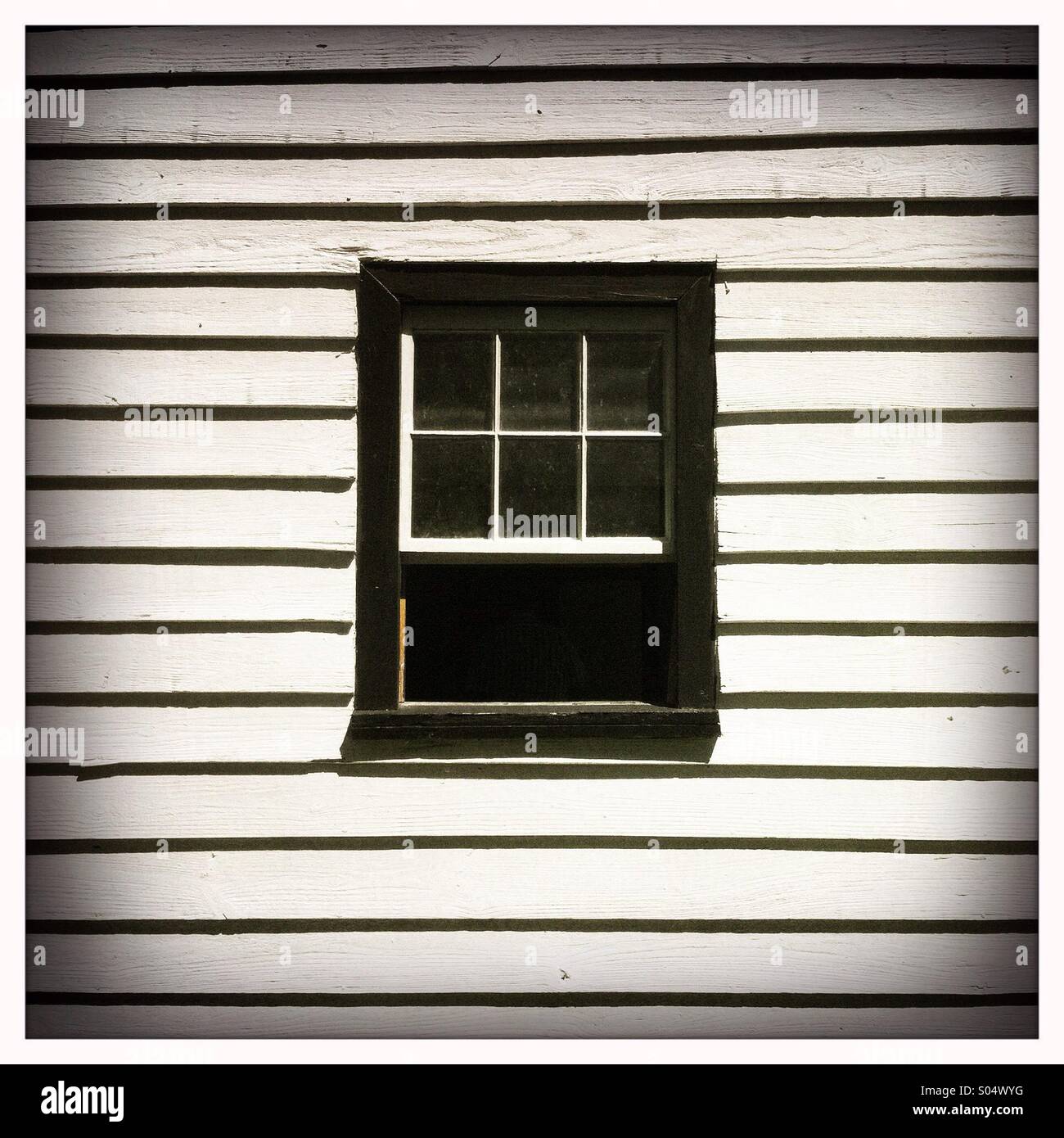 Una ventana negra casa enmarcada en una pared de madera blanca Foto de stock