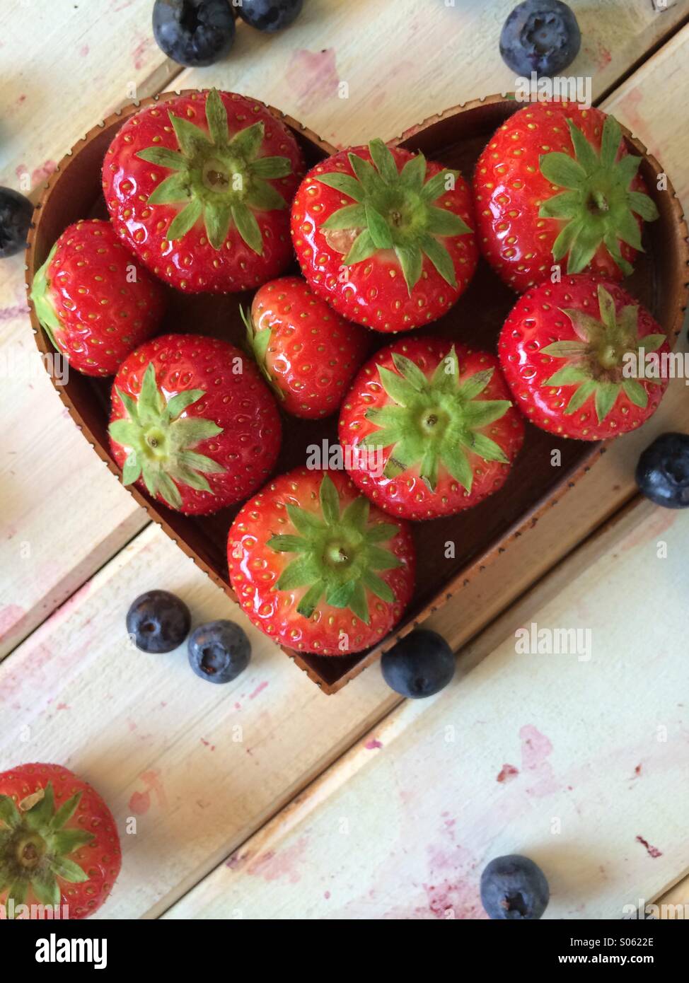 Fresas frescas en forma de corazón el amor del canasto y los arándanos en vintage en estilo retro de fondo de tabla Foto de stock