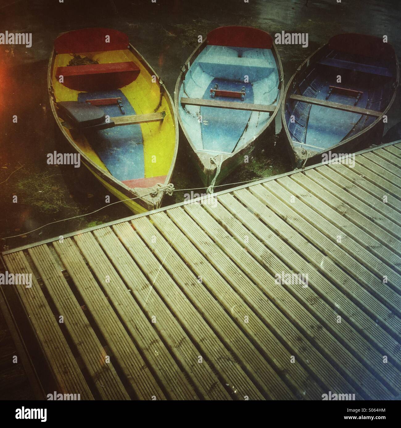 Tres coloridos botes a remo amarrado en un muelle de madera Foto de stock