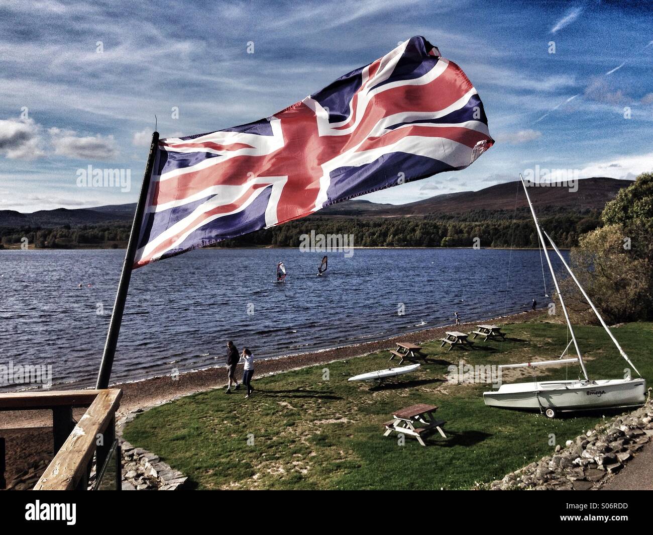 Bandera Union Jack tiro contra un escocés loch lake donde hay surfistas. Formato horizontal. Foto de stock