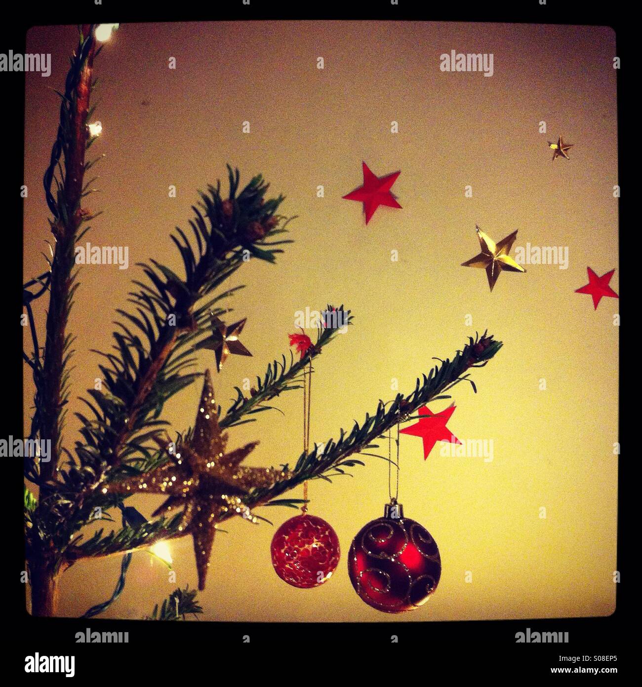 Detalle de un árbol de navidad decorado con bolas y las luces de hadas, con rojo y estrellas de oro en el fondo Foto de stock