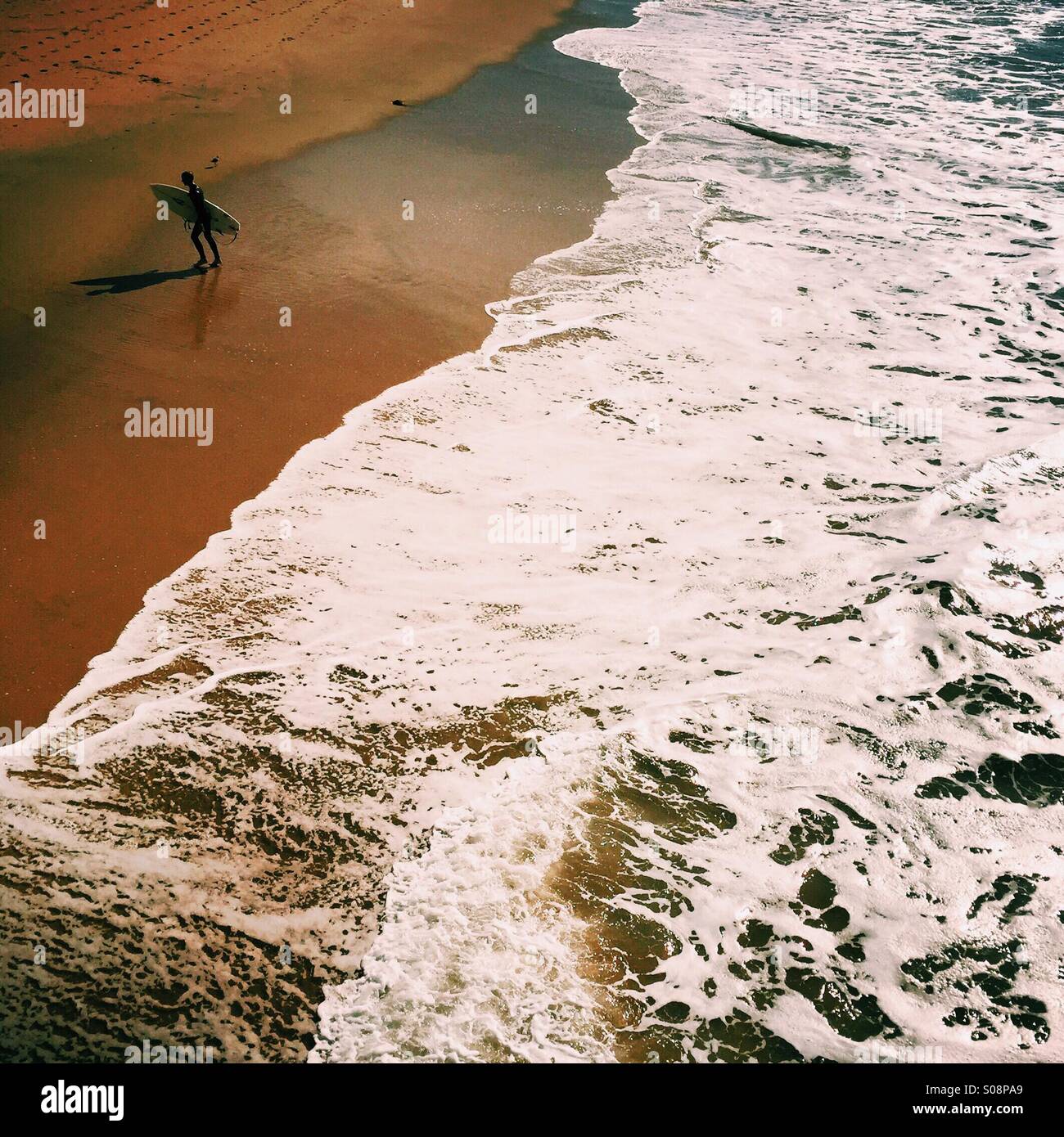 Un surfista masculino caminatas hasta la playa. Manhattan Beach, California, USA. Foto de stock