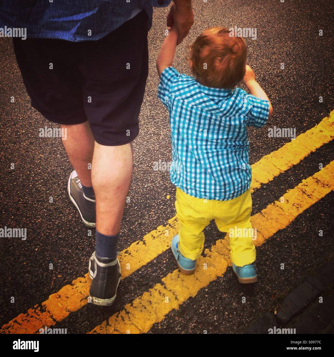 El padre y el hijo caminando a través de líneas amarillas dobles en una carretera en Londres. Foto de stock