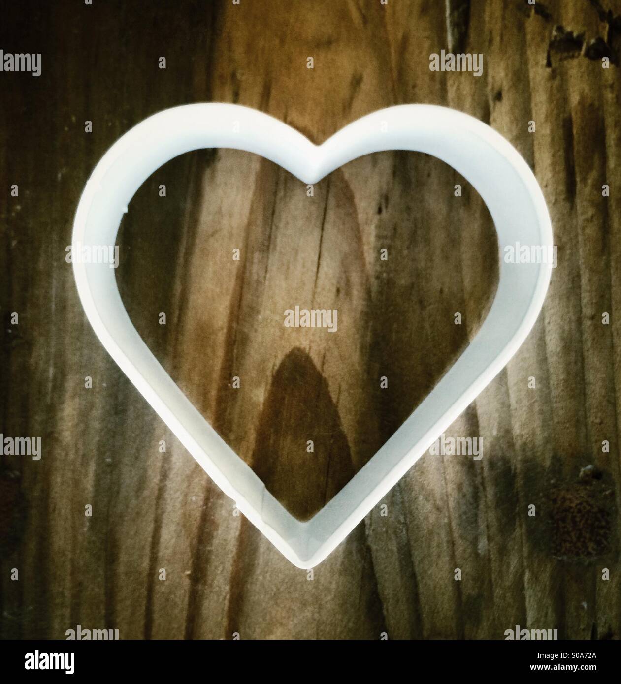 En forma de corazón blanco cookie cutter sobre la tabla de cortar de madera Foto de stock