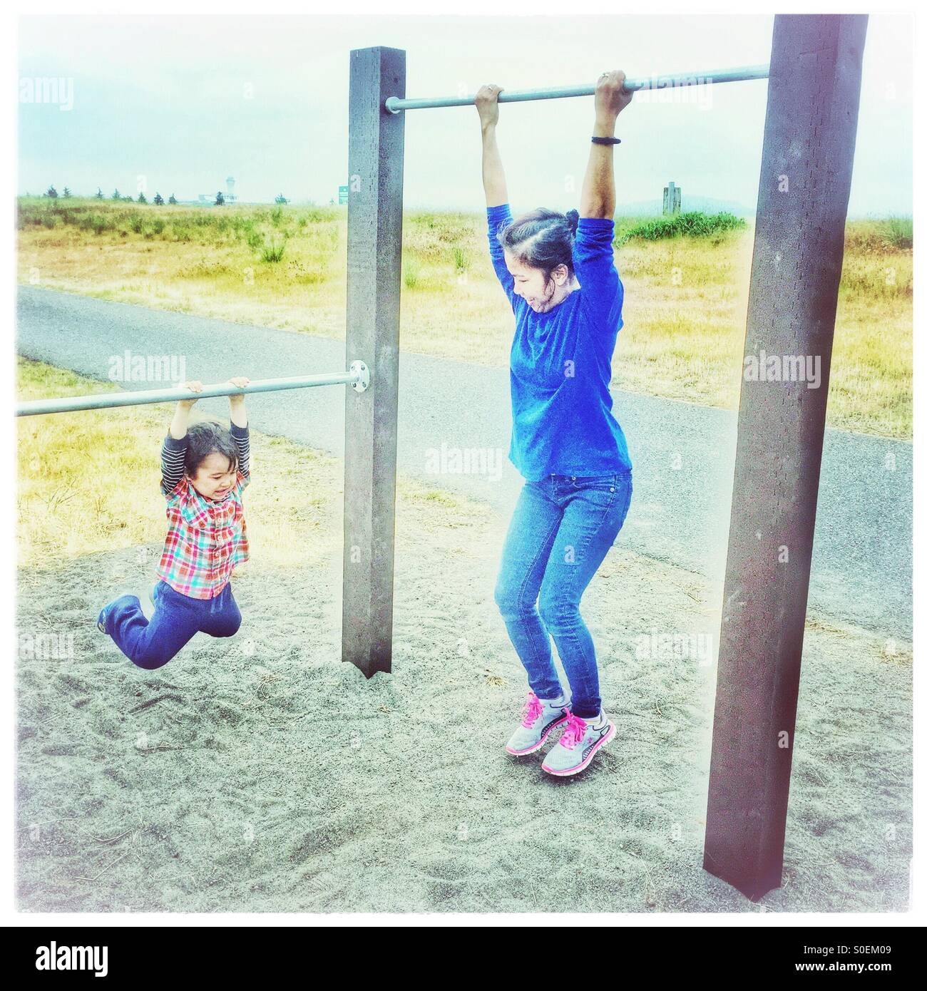 Una madre y un niño cada encontrar contiguas a los bares de pull-up su tamaño para el ejercicio y la diversión al aire libre cerca de un camino. Foto de stock