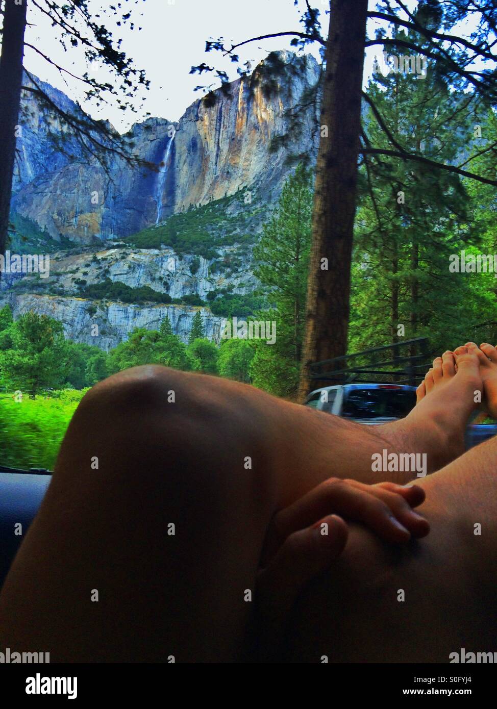 Un joven adulto se relaja con sus pies fuera de la ventanilla mientras admira en Cataratas de Yosemite Foto de stock