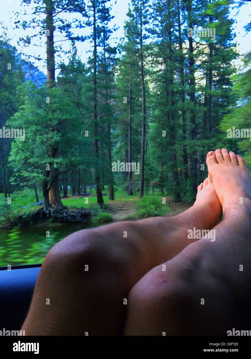 Un joven adulto se relaja con sus pies fuera de la ventana mientras miran a Merced Creek Foto de stock