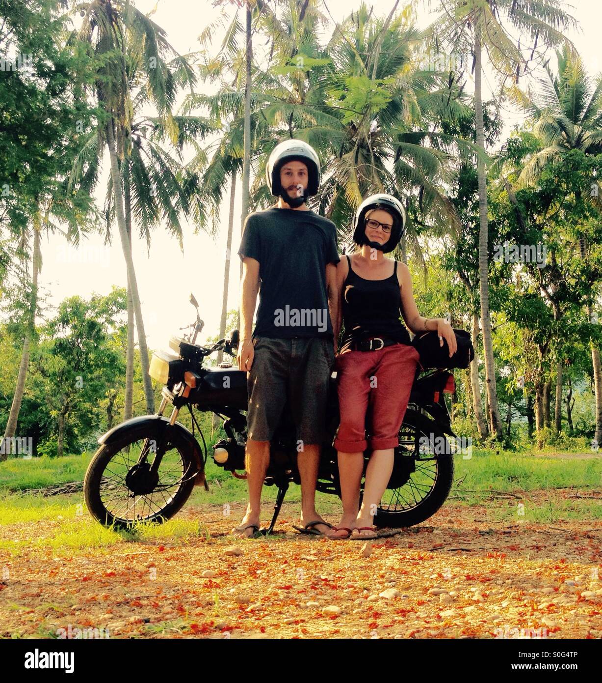 Una pareja con su moto, dos personas de pie delante de una motocicleta vintage en una ubicación tropical, Luang Prabang, Laos, Asia Foto de stock