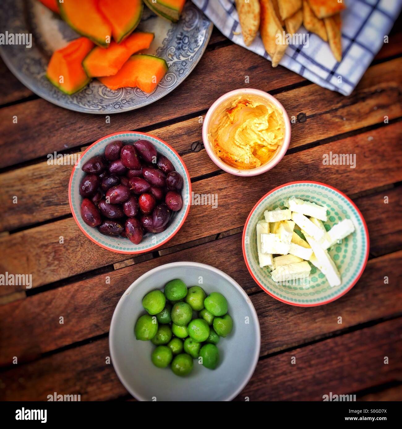 Aceitunas, houmous, queso y melón sobre una tabla de madera Foto de stock