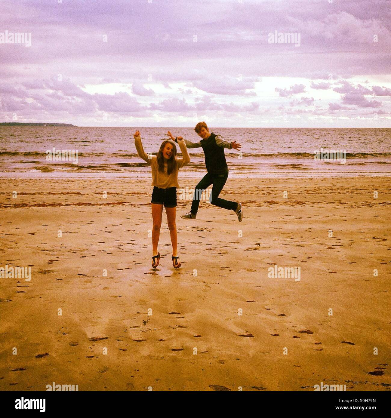 Chico y chica saltando en la playa Foto de stock