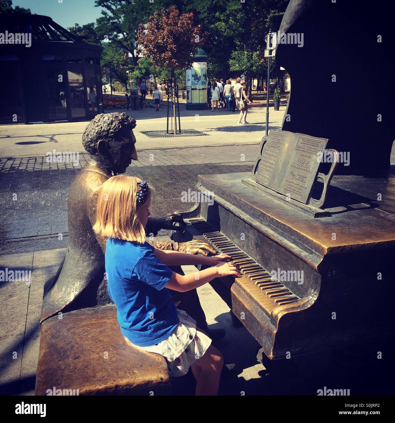 Niña sentada junto a la estatua de un famoso compositor polaco Moniuszko, sobre la calle Piotrkowska, en Lodz, Polonia, simulando tocar su piano junto a él Foto de stock